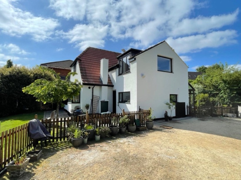 The same house from the driveway, white render with dark windows
